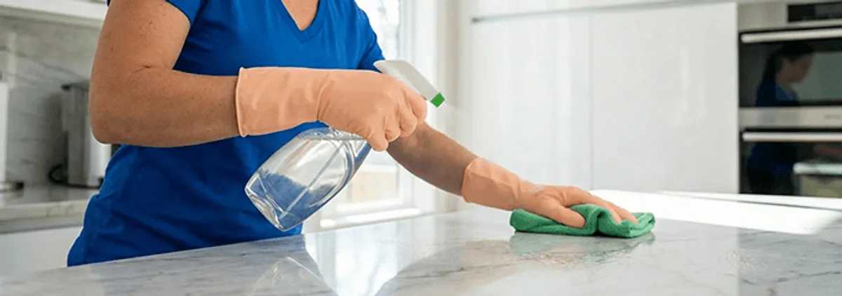 Maid service worker spraying and wiping a kitchen countertop with a microfiber cloth for sanitizing, Saint Petersburg, FL.